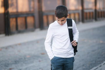 Teenage boy take out a wireless headphones and put then into the ears. Young boy in white shirt with backpack. Boy listen music