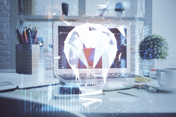 Computer on desktop in office with bulb icon hologram. Double exposure. Concept of idea.
