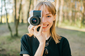 Portrait of beautiful young female photographer with short fair hair in black t-shirt stands with her camera and smiles