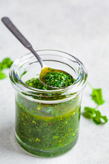 Fresh traditional chimichurri sauce for barbecue meat in glass jar, light background.