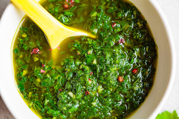 Fresh traditional chimichurri sauce for barbecue meat in a white bowl, light background, top view.
