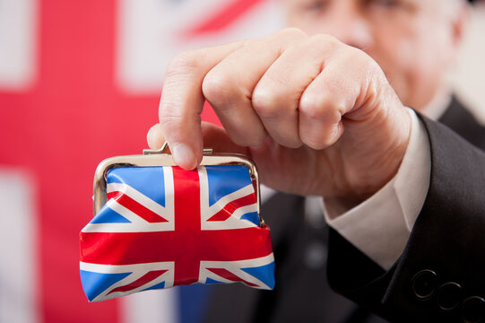 Stereotypical English businessman holding a Union Jack money purse. The man is wearing a dark business suit and bowler hat, with a Union Jack flag background.