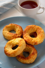 Appetizing baked bagels on a blue plate on a white wooden background with a white mug of tea and a kitchen towel