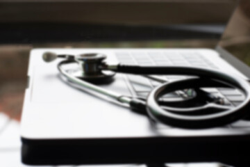 Blurred image of medical stethoscope and  laptop computer isolated on dark table background with reflection. Medic tech, online medical, emr, telehealth concept. 