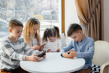Children sit at a table in a cafe and play mobile phones together. Modern entertainment