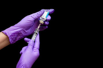 Fototapeta na wymiar Doctor hands with rubber gloves holding disposable plastic syringe and drawing liquid drug from vial for medical injection isolated on dark background. 
