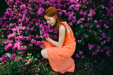 Picture of an amazing red-haired baby girl in an orange dress enjoying a pastime in the big spring garden