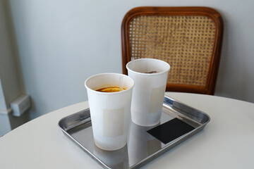 Paper cups of iced coffee on aluminium tray and white table