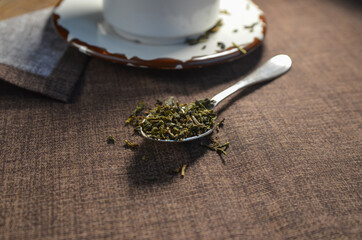 Silver spoon with leafy green tea on a brown napkin with space for text