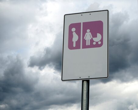 Expectant mothers only parking sign. Mothers with babies  parking sign .  Pink and white signpost on cloudy sky background. Copy space.