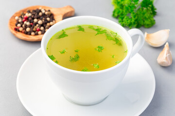 Chicken broth in  white cup garnished with chopped parsley, vertical, horizontal