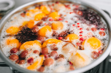 Fresh fruits: apricots, cherries, raspberries, apples are boiled in boiling water in a metal pan on a stove with bubbles and foam close-up. Cooking delicious homemade compote. Photography, concept.