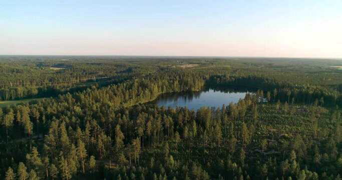 Aerial view around a reflecting pond, in a forest, during golden hour, on a sunny, summer evening, in Uusimaa, Finland - orbit, drone shot