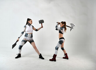 beautiful girls in costumes of robots quarreled and fight with a battle ax and a war hammer