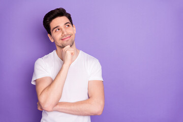 Photo of attractive handsome guy good mood arm on chin dreamer look interested empty space intelligent creative person wear casual white t-shirt isolated purple pastel color background