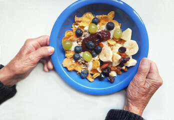breakfast for senior woman. old hands holding blue plate with cereal and fresh fruits