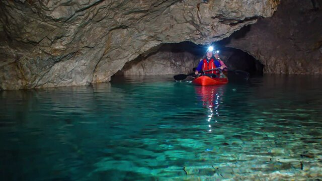 Caucasian women paddle on kayak in underground rocky mining tunnel in crystal clear fresh shallow water towards camera, Podzemlje Pece, Mezica, Slovenia, static