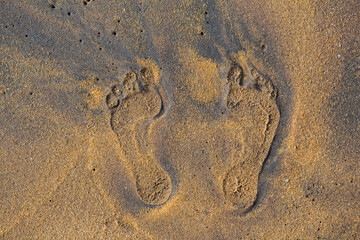 Fototapeta na wymiar filled frame close up background wallpaper shot of human foot prints on a yellow sand beach surface forming beautiful patterns and shapes