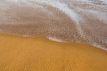 Fototapeta na wymiar beautiful filled frame close up seascape wallpaper background shot of golden orange sand with white foamy waves of the Indian ocean forming pretty textures and patterns. Pitiwella beach, Sri Lanka