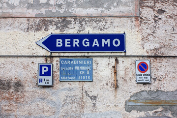 Wegweiser nach Bergamo und andere Schilder an alter Hauswand in Italien.