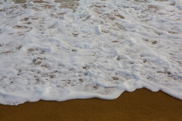 beautiful filled frame close up seascape wallpaper background shot of golden orange sand with white foamy waves of the Indian ocean forming pretty textures and patterns. Pitiwella beach, Sri Lanka