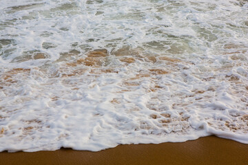 beautiful filled frame close up seascape wallpaper background shot of golden orange sand with white foamy waves of the Indian ocean forming pretty textures and patterns. Pitiwella beach, Sri Lanka