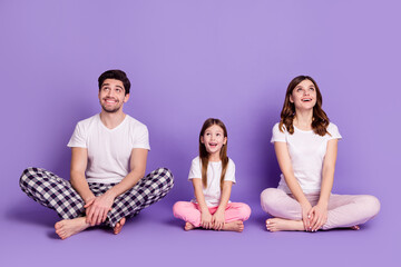 Portrait of cheerful glad family dad mom offspring daughter wearing cozy cotton pajama sitting on...