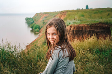 Little girl child sitting in nature on the grass in front of the river