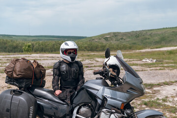 Girl motorcyclist in a helmet. Dressed in a jacket with a turtle, body armor, knee pads. Traveling is an extreme hobby. Safety and body protection. Bike with bags.
