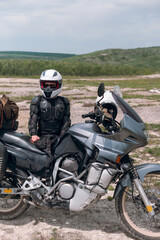 Fototapeta na wymiar Girl motorcyclist in a helmet. Dressed in a jacket with a turtle, body armor, knee pads. Traveling is an extreme hobby. Safety and body protection. Bike with bags. vertical photo