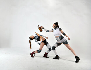 beautiful girls in costumes of robots quarreled and fight with a rolling pin and a big bottle