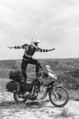 Extreme stunt on a bike. Like surfing. Motorcycle driver wearing a turtle jacket, body armor and a helmet. Stands on top. Vertical photo. Black and white