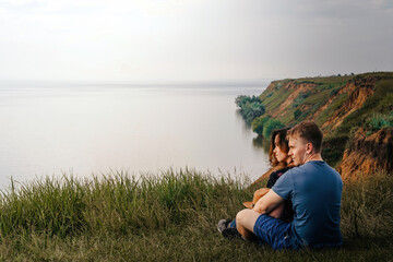 Fototapeta premium A back view of young adult lovers sitting on the edge of a cliff and watching the sea on a rainy and gloomy day. the concept of travel.