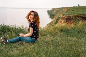 A young girl with long hair sits on the edge of a cliff overlooking the sea, a concept for traveling