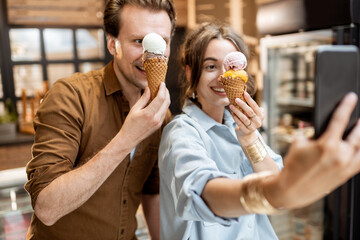 Young and cheerful couple making selfie photo with yummy ice cream in waffle cones, having fun...