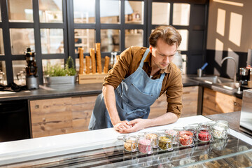 Confectioner trying different food additives in the form of topping for ice cream at the counter of a shop