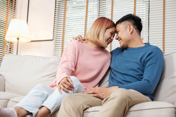 Happy asian couple sitting on sofa after unpacking cardboard boxes  while moving to new home at sofa in living room.new house relocation