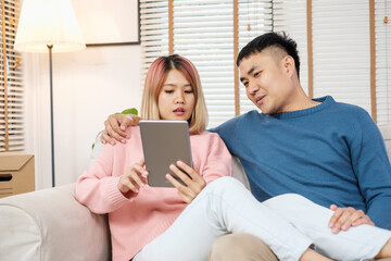 happy asian couple using tablet to design decorate new house interior at sofa when finish moving box in house