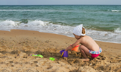 Fototapeta na wymiar The little girl plays on the seashore with sand. Summer fun. 