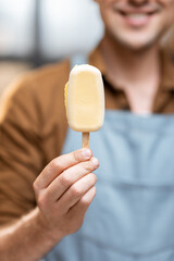 Portrait of a handsome seller in uniform with white chocolate ice cream on a stick at the shop, close-up