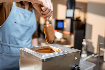 Seller dips ice cream into the hot melted chocolate, making ice cream on a stick with toppings