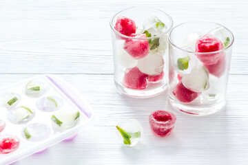Cocktail glasses with berries in ice cubes on white table