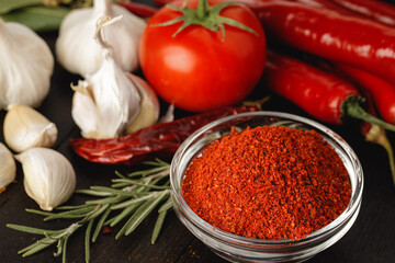 Red chili spice in glass bowl with herbs on dark table