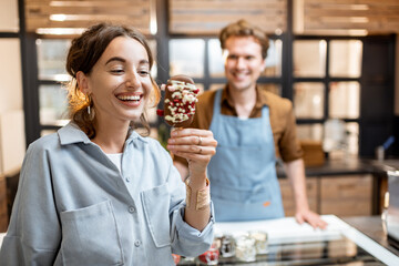 Young and joyful woman with a yummy chocolate ice cream at the shop with seller on the background