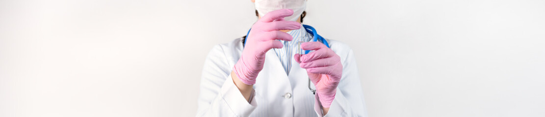 Cropped view of young female doctor in a white coat, in a medical mask and pink sterile gloves holding ampoule vaccines for children or older adults. Concept: diseases, medical care, diabetes.