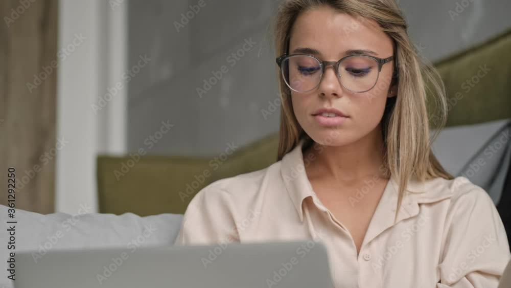 Wall mural concentrated attractive blonde woman in eyeglasses using laptop computer while sitting on the floor 