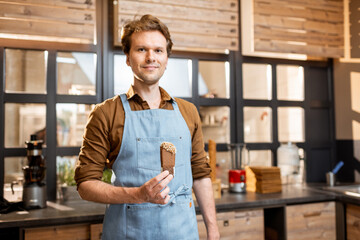 Portrait of a handsome seller in uniform holding chocolate ice cream in a shop