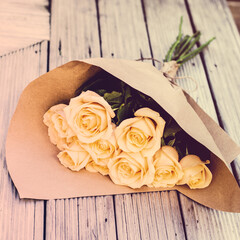 Retro style photo of beautiful peach-coloured roses wrapped in brown paper on a wooden bench