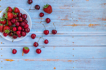 Composition of fresh cherries, strawberries. Bright cherries and strawberries lie on a white plate and a blue wooden background. Summer. Fruits.