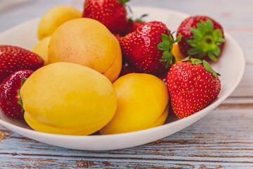 Fruits on a white plate on a wooden background. Strawberries and apricots on a white plate. A set of fruits.